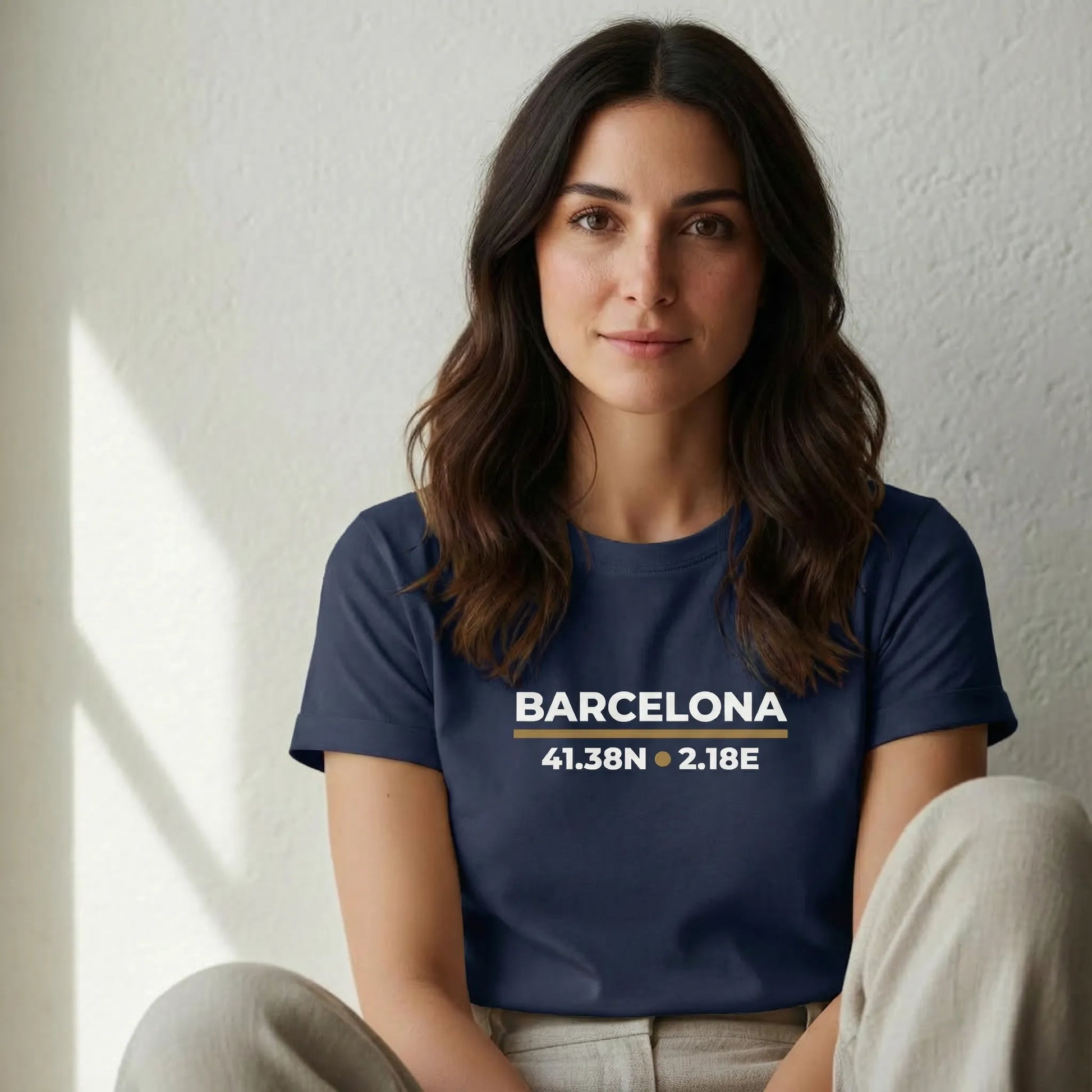 TP:HERO Woman wearing a navy blue t-shirt with 'Barcelona' and coordinates printed on it, sitting against a white wall.