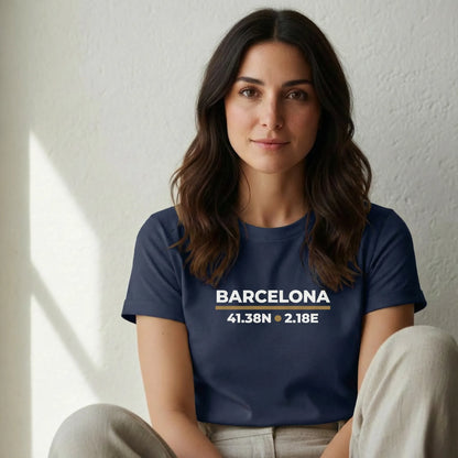 TP:HERO Woman wearing a navy blue t-shirt with 'Barcelona' and coordinates printed on it, sitting against a white wall.