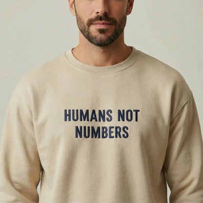 Man wearing a beige sweatshirt with 'HUMANS NOT NUMBERS' text on a plain background