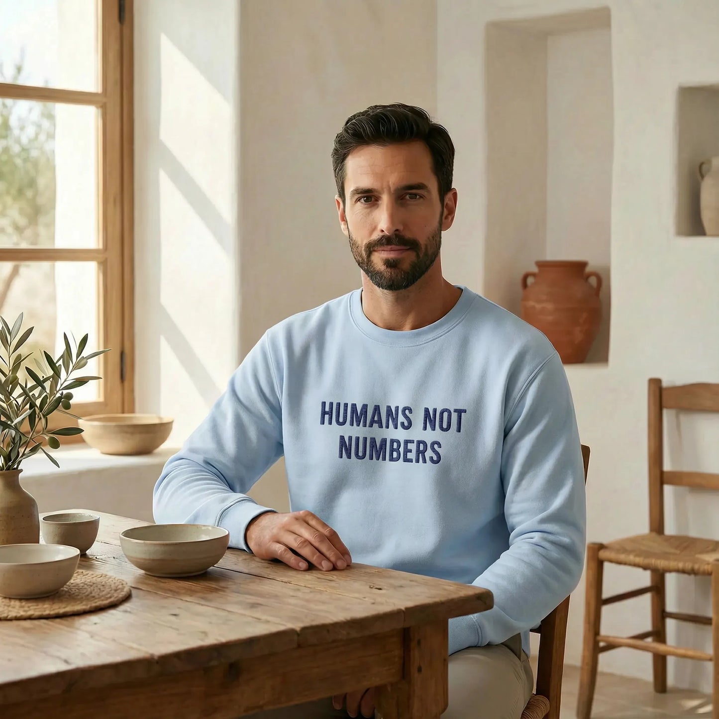 Man wearing a light blue sweatshirt with 'HUMANS NOT NUMBERS' text in a home setting.