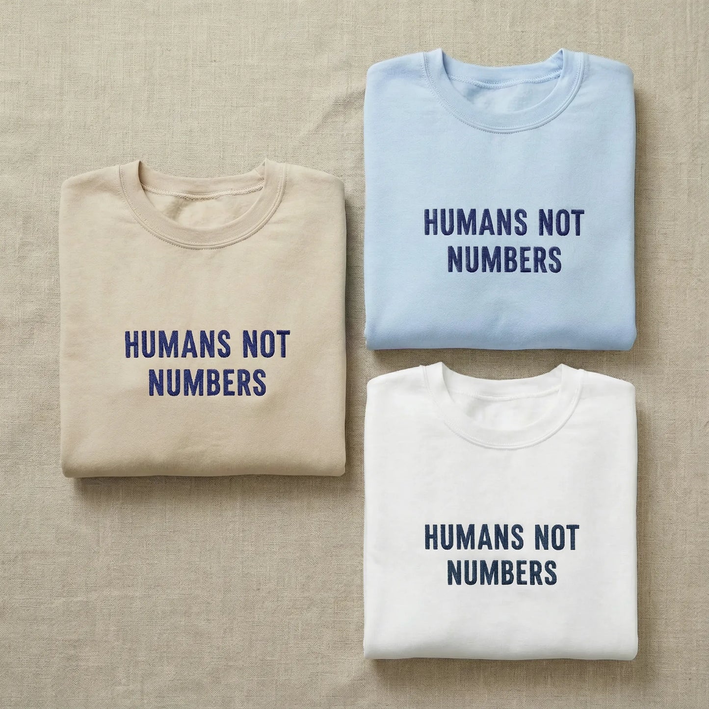Three folded shirts with 'Humans Not Numbers' text on a beige fabric background