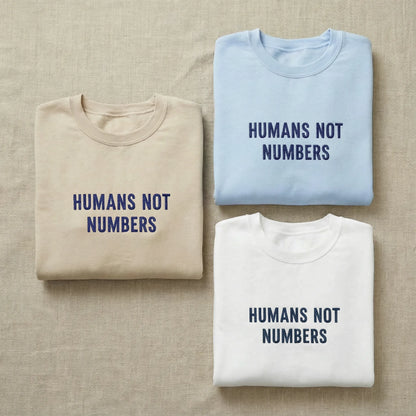 Three folded shirts with 'Humans Not Numbers' text on a beige fabric background