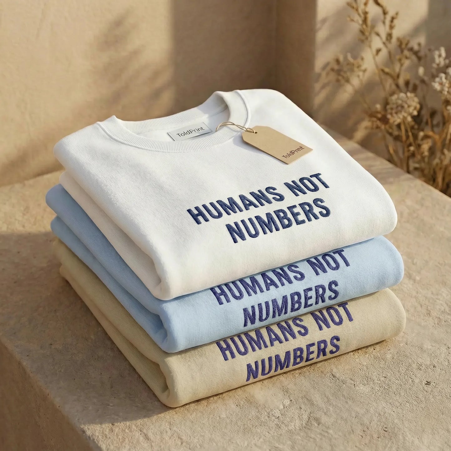 Stack of sweatshirts with 'Humans Not Numbers' text on a neutral background