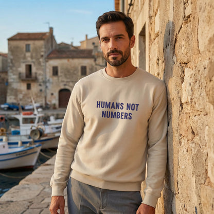 Model wearing sand Humans Not Numbers embroidered sweatshirt outdoors in Mediterranean street.