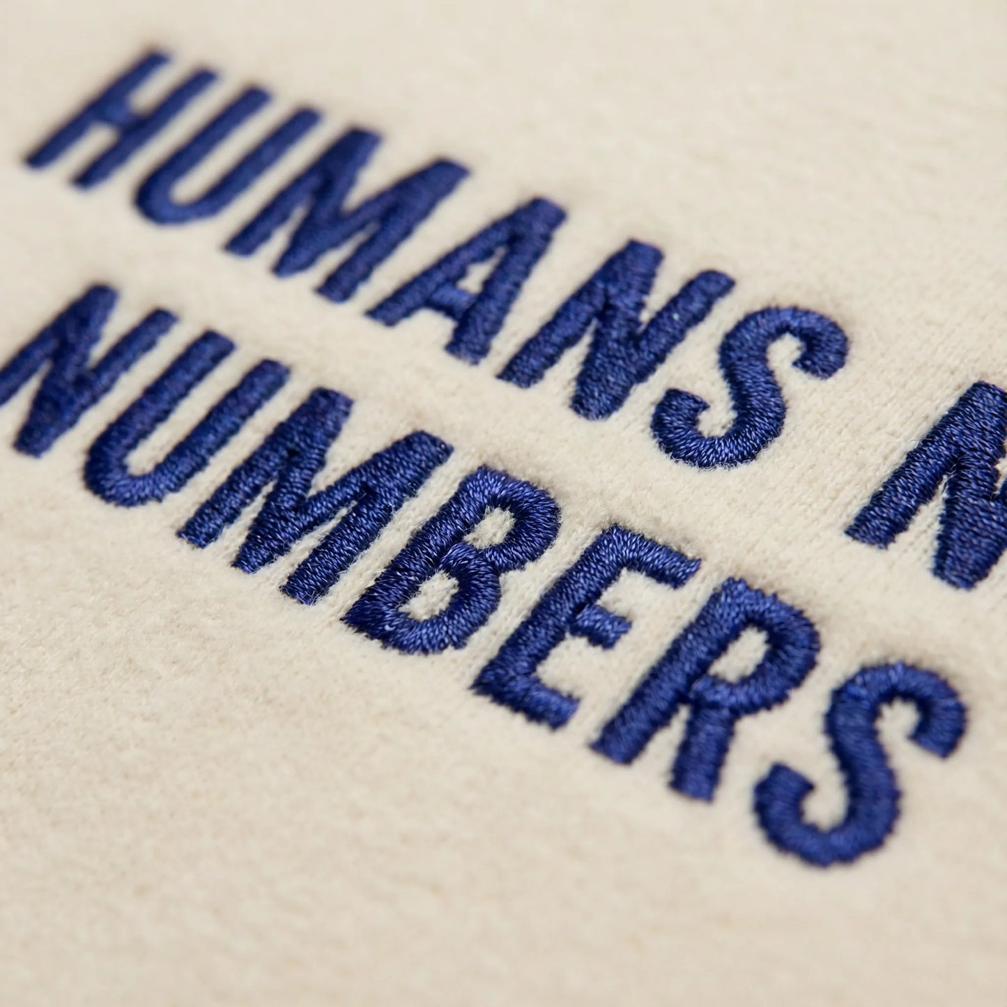 Macro close up of Humans Not Numbers embroidered sweatshirt in sand with deep blue thread