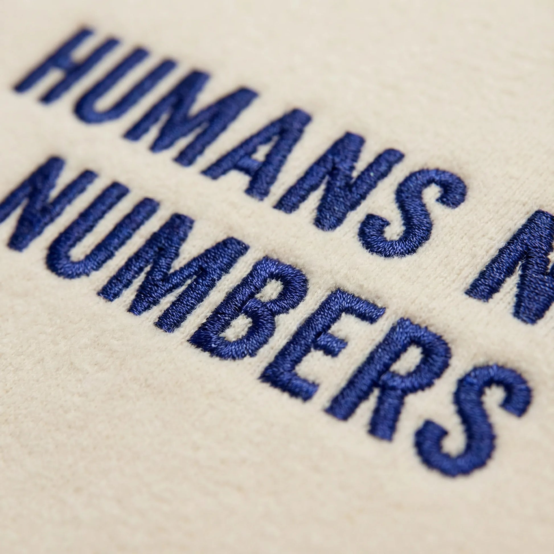 Macro close up of Humans Not Numbers embroidered sweatshirt in sand with deep blue thread