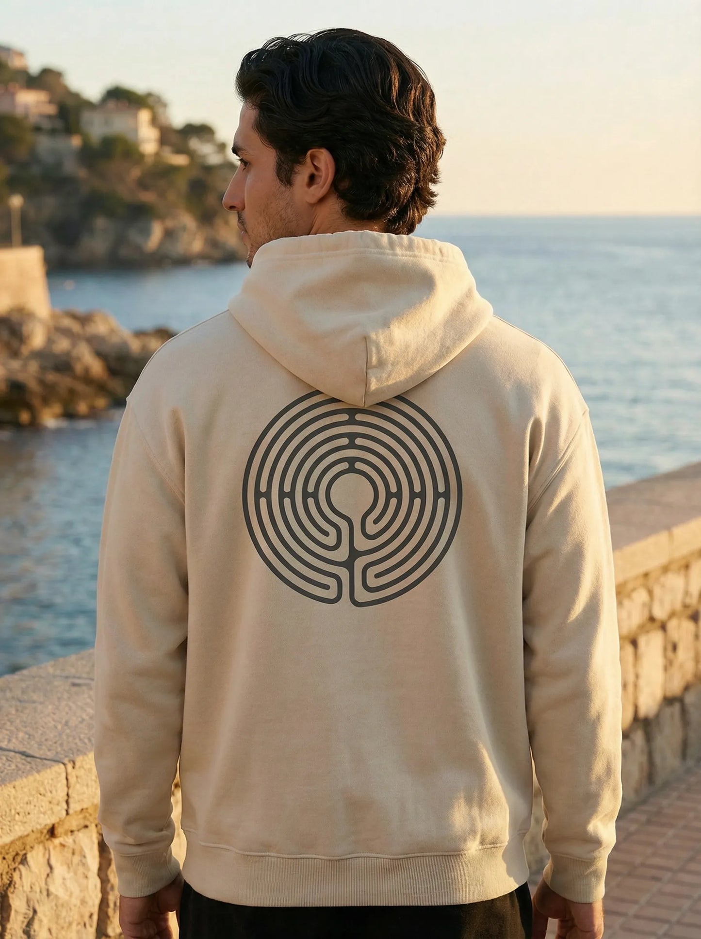 Model by the sea wearing Labyrinth Hoodie with back labyrinth design visible