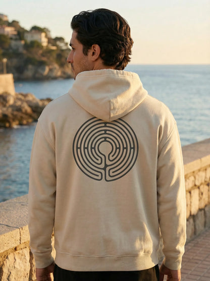 Model by the sea wearing Labyrinth Hoodie with back labyrinth design visible
