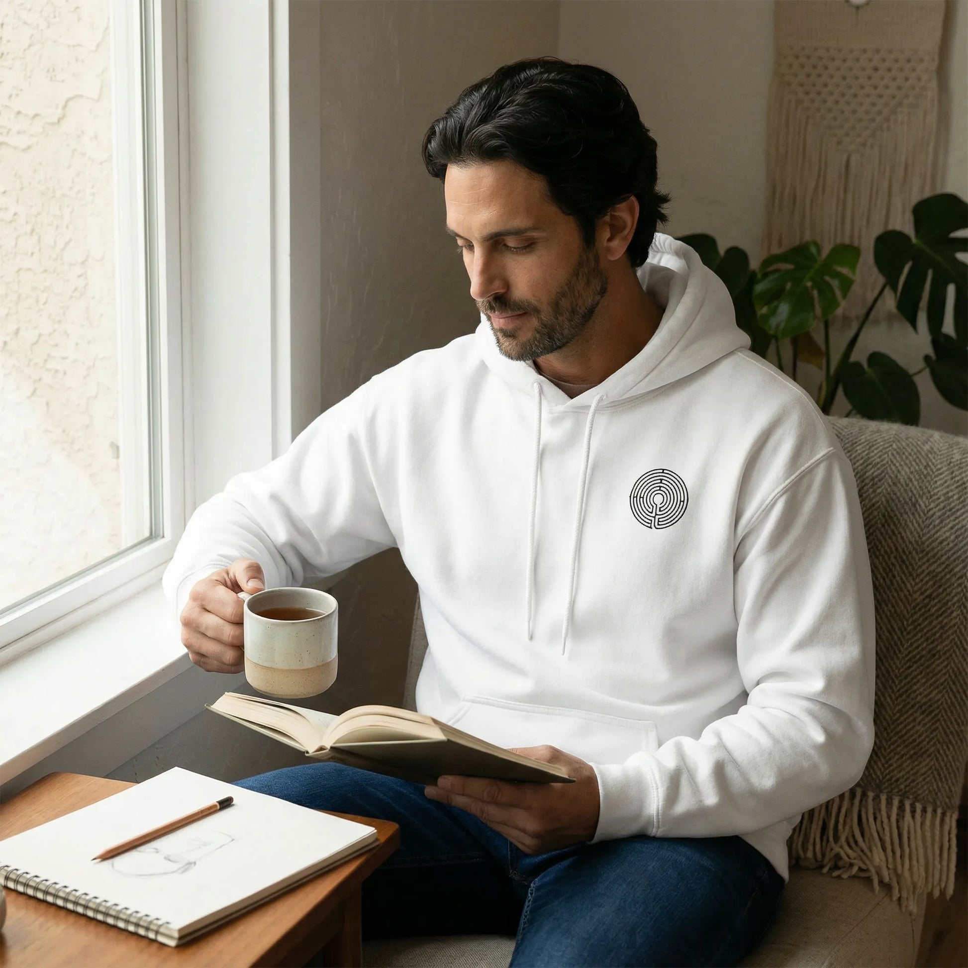 Indoor calm scene showing front chest glyph and relaxed unisex fit of Labyrinth Hoodie