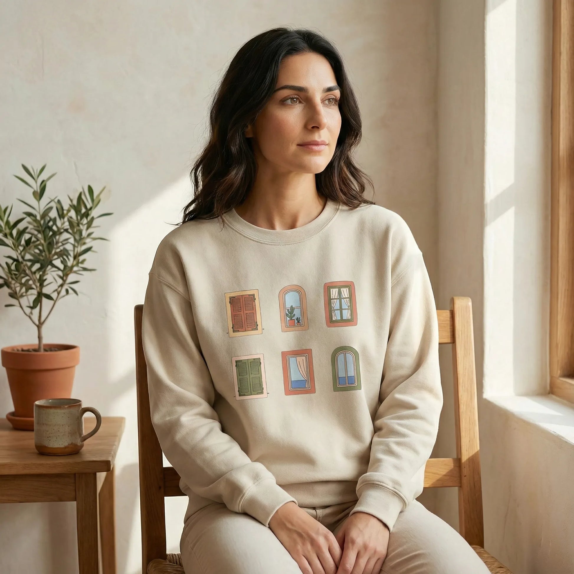 Woman wearing a beige sweatshirt with window designs, sitting in a sunlit room.