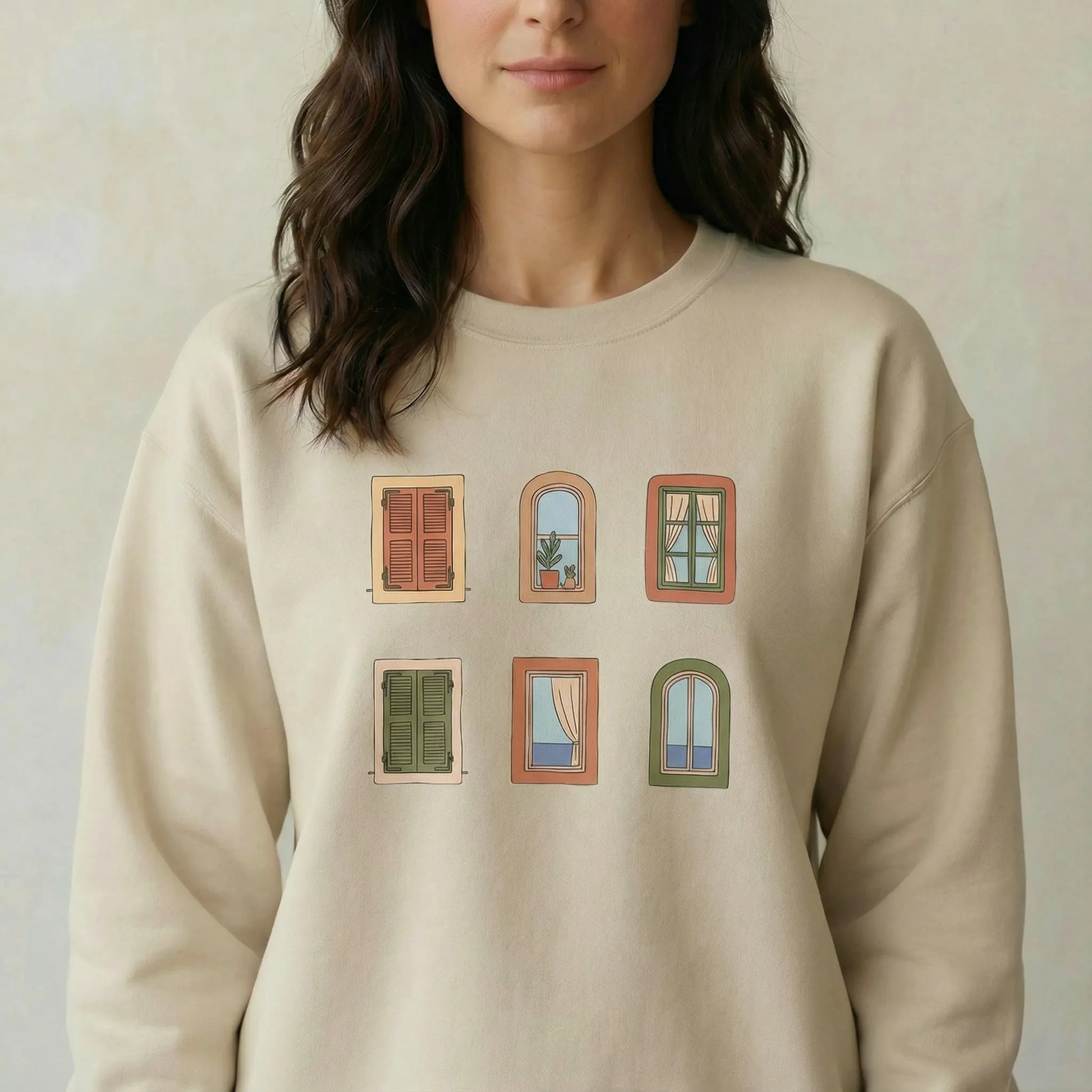 Person wearing a beige sweatshirt with window illustrations on a plain background