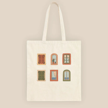 Top-down flat lay of the Mediterranean Windows natural cotton tote bag on a neutral beige fabric surface