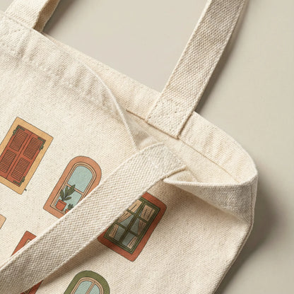 Close-up of the natural cotton Mediterranean Windows tote bag showing the handle and stitching where the strap joins the body of the bag.