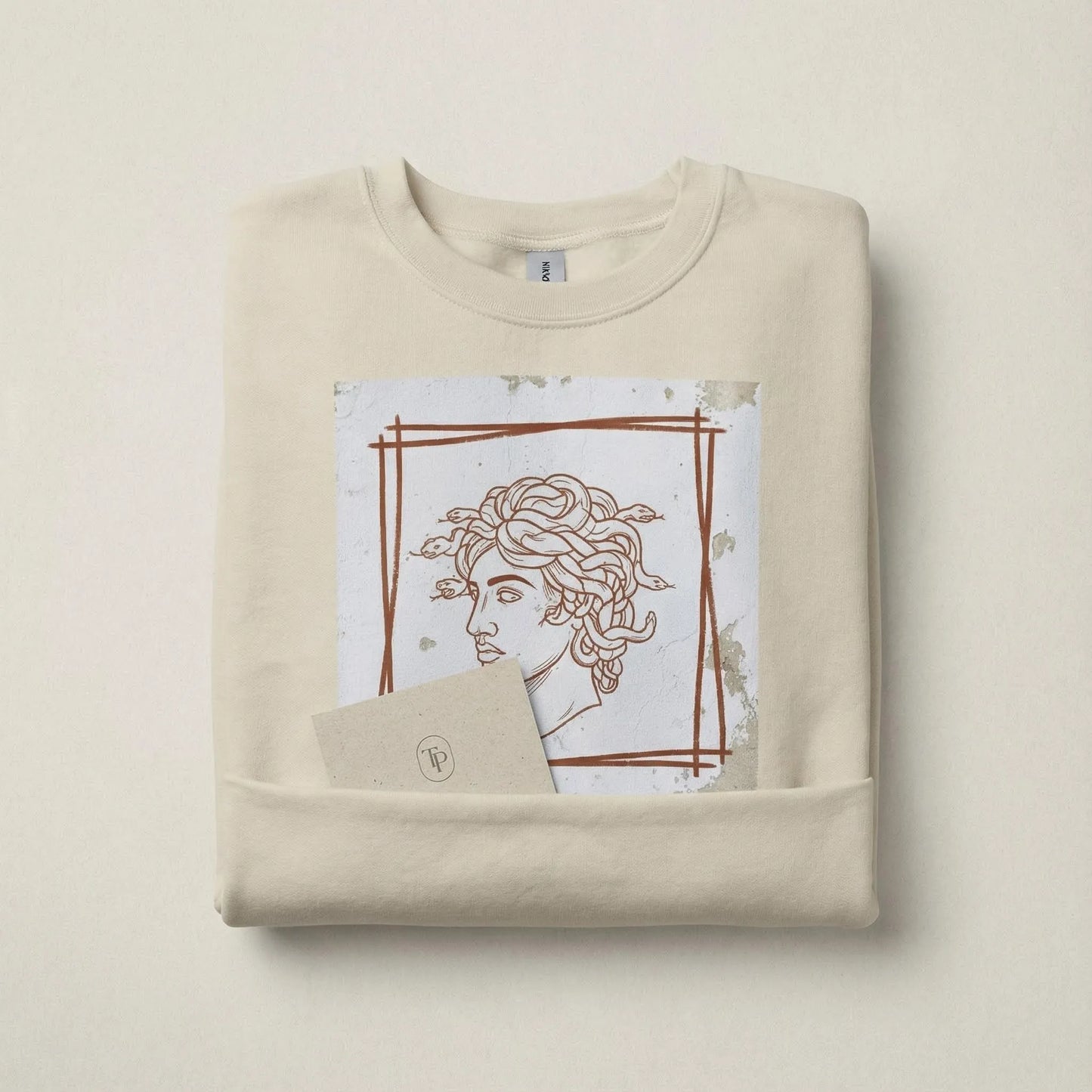 Folded Sand Minimal Medusa sweatshirt with artwork visible in a minimal brand scene
