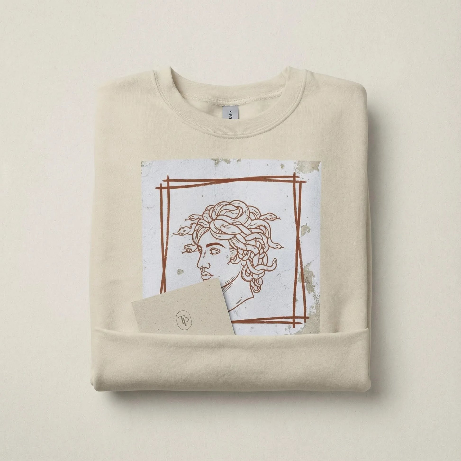 Folded Sand Minimal Medusa sweatshirt with artwork visible in a minimal brand scene