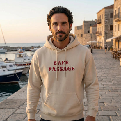 Unisex model wearing Safe Passage embroidered hoodie by Mediterranean seaside promenade