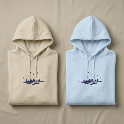 Sea Crossing hoodie colour options shown together in sand and light blue with matching navy chest embroidery.