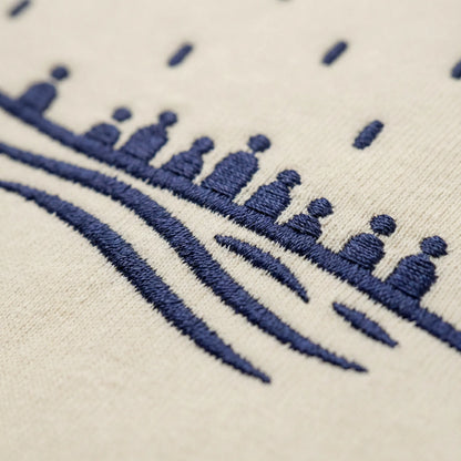 Macro detail of navy embroidery stitching on the sand Sea Crossing hoodie, showing thread texture.