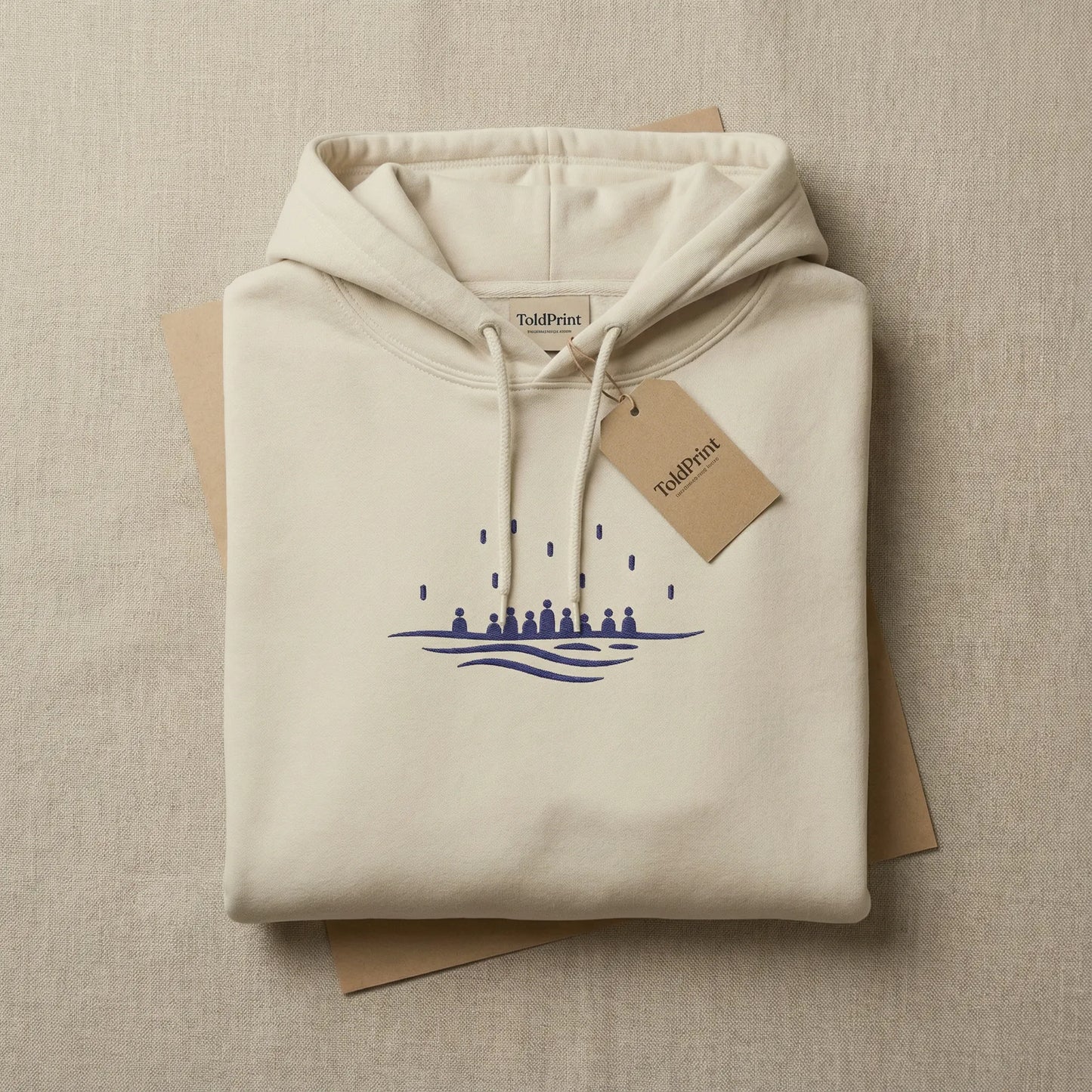 Folded sand Sea Crossing hoodie with ToldPrint label and navy embroidery visible on the top fold.