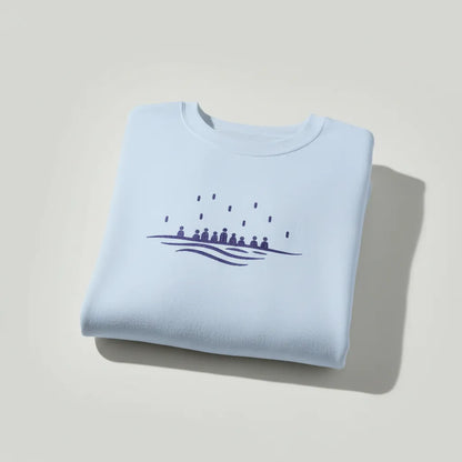 Folded light blue crewneck sweatshirt showing embroidered sea motif, minimalist Mediterranean style