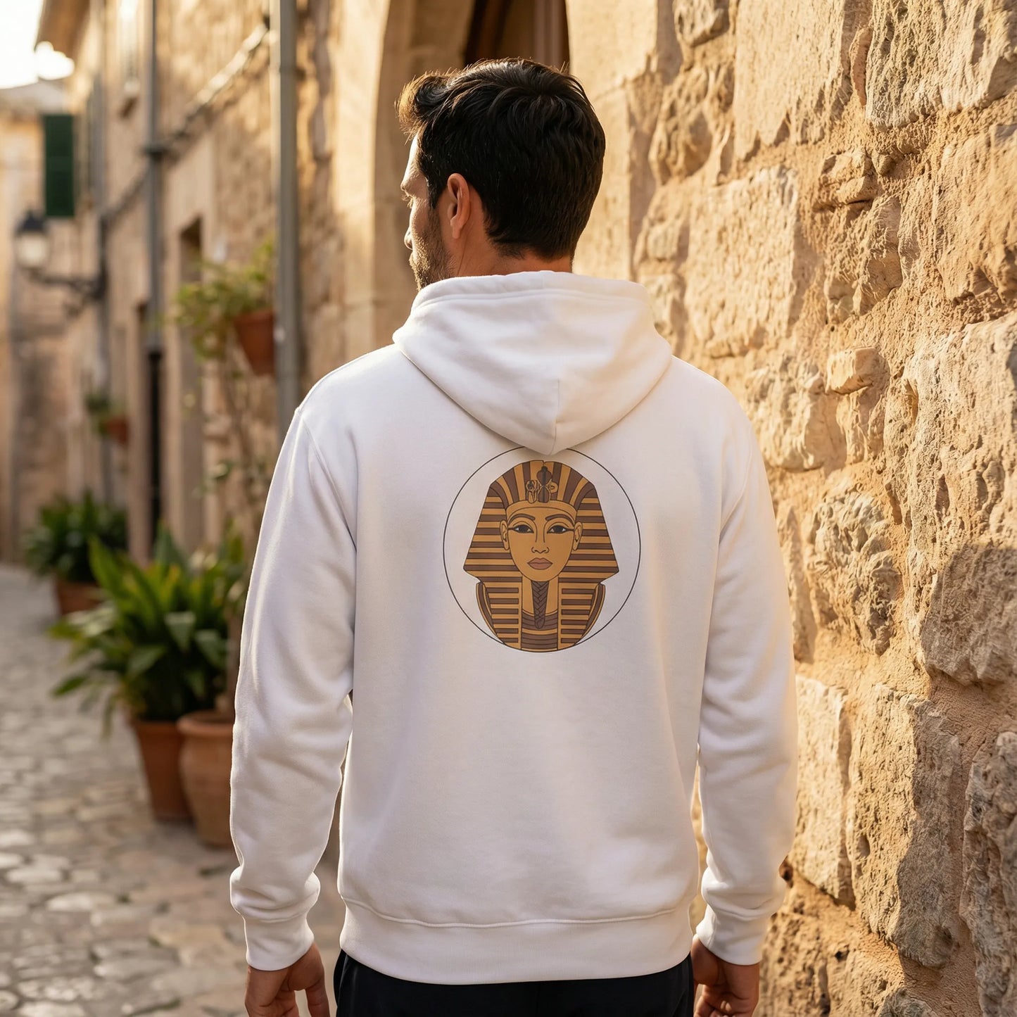 Person wearing white Sphinx graphic hoodie outdoors, back view with large Sphinx print, warm Mediterranean light