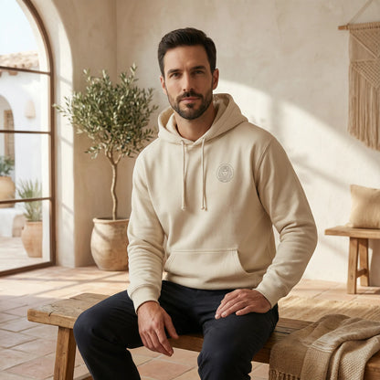Unisex model indoors wearing sand Sphinx hoodie, front view with minimal chest badge and relaxed styling