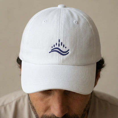 Close-up of navy embroidered waves emblem on white dad cap while worn, stitch detail and front panel texture.