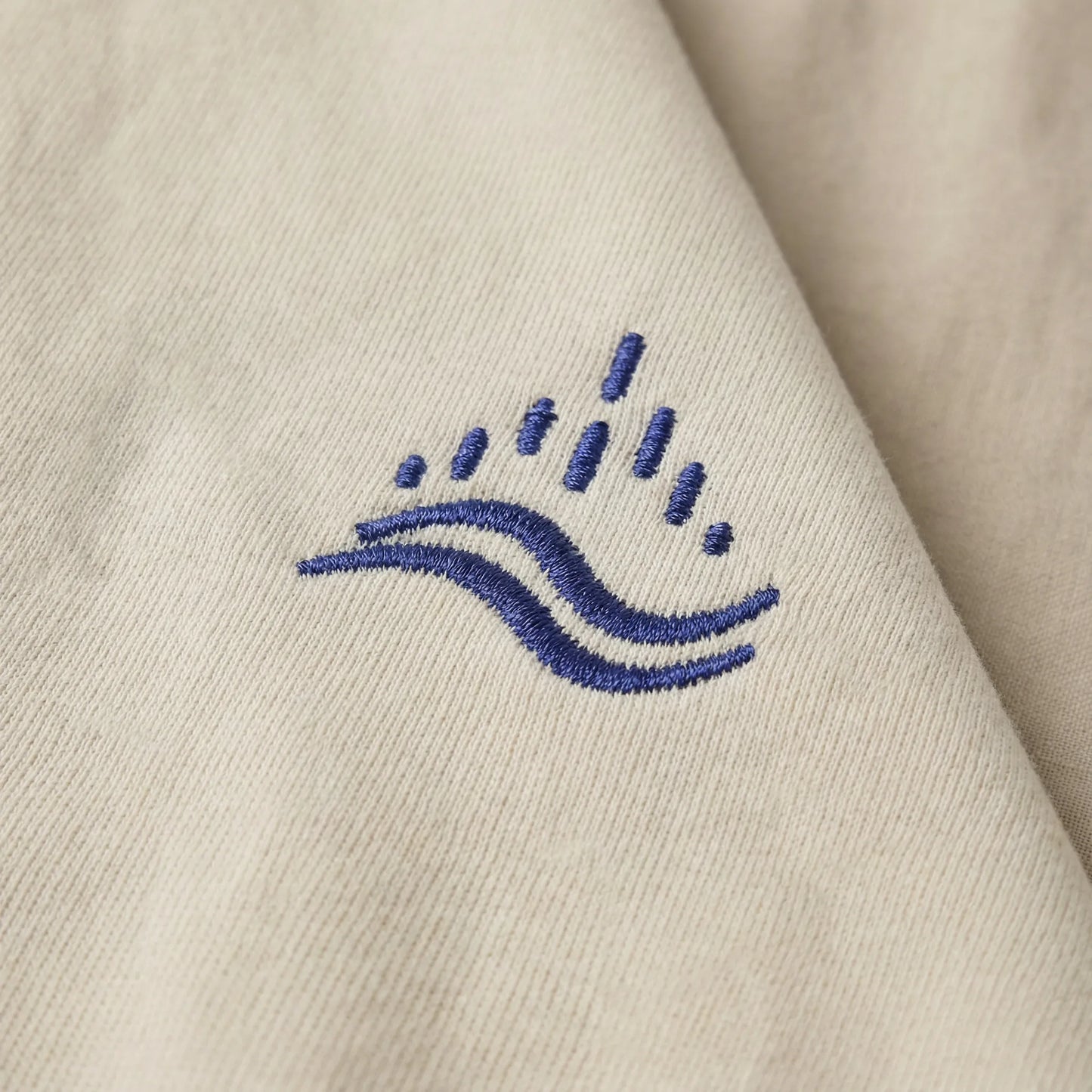 Detailed close-up of the navy waves emblem embroidery on sand sweatshirt.