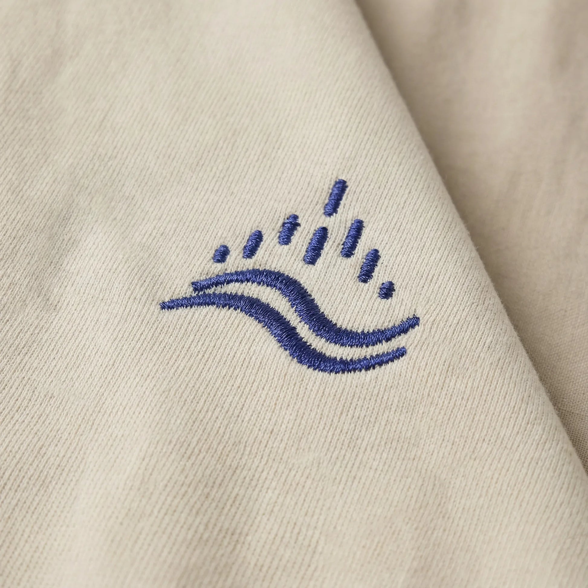 Detailed close-up of the navy waves emblem embroidery on sand sweatshirt.