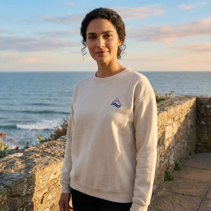 Outdoor Mediterranean scene with model wearing sand sweatshirt featuring navy waves emblem.