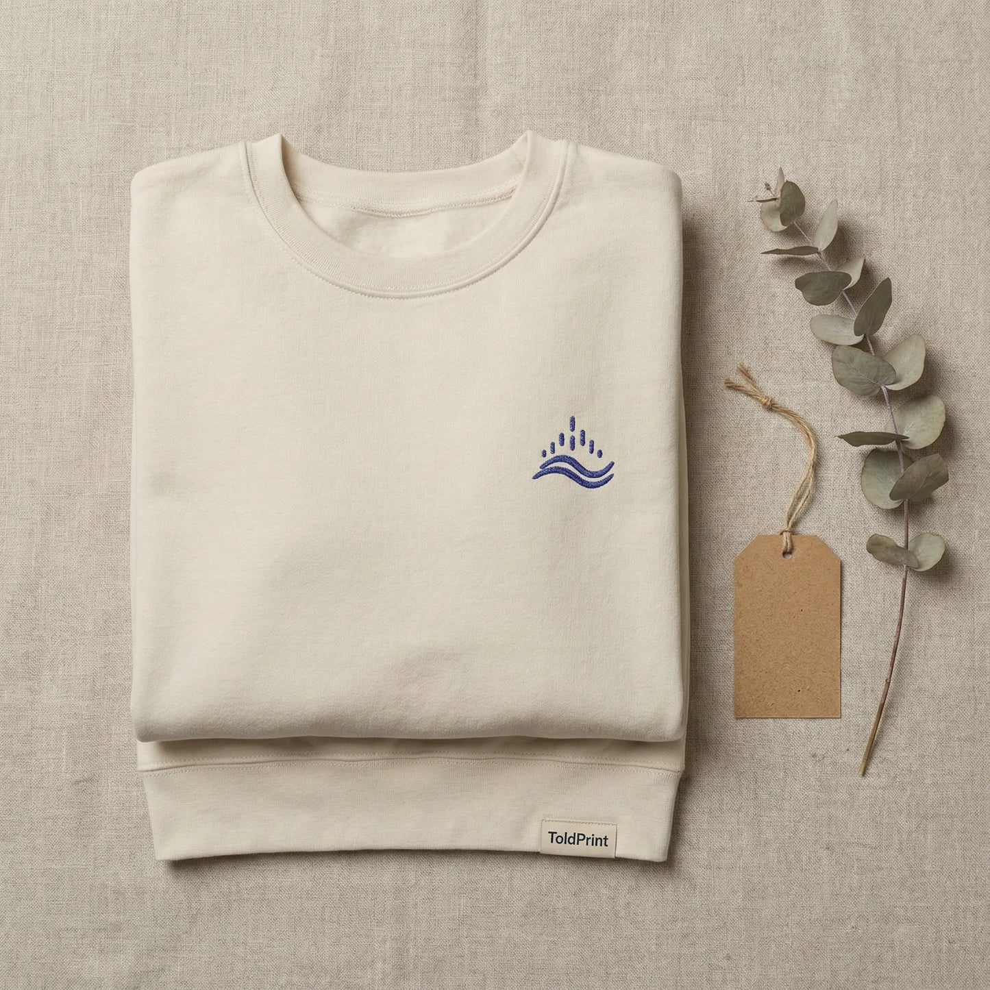 Folded sand waves emblem sweatshirt with ToldPrint label and visible navy embroidery.