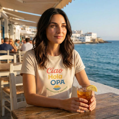 Model wearing Ciao Hola OPA t-shirt at a seaside café with Mediterranean vibe