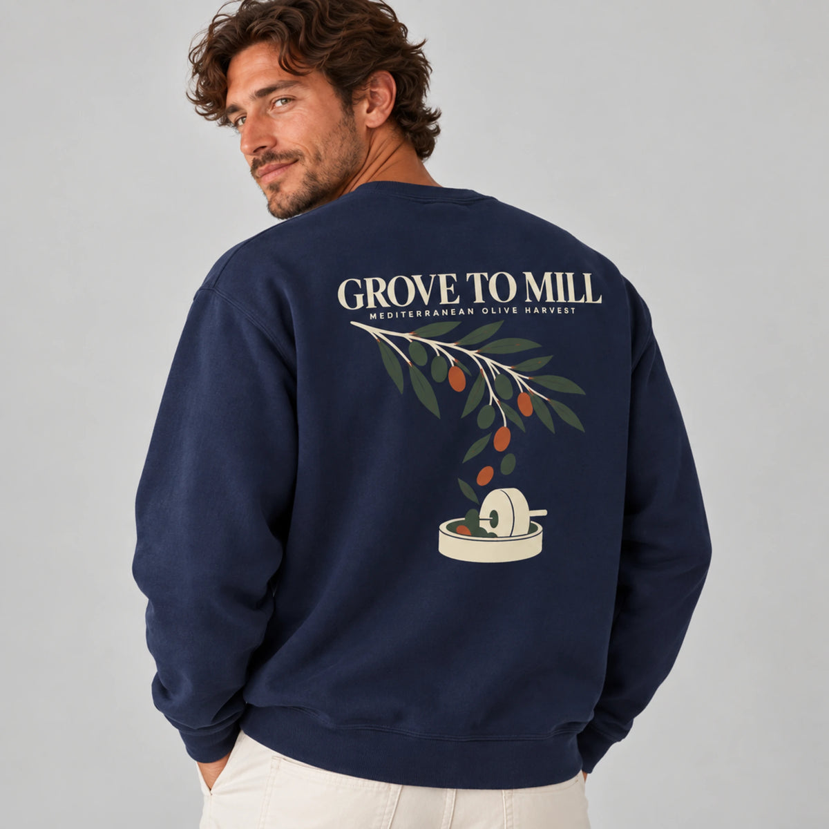 Male model wearing the True Navy Grove to Mill sweatshirt from the back, featuring the Mediterranean Olive Harvest back print with olive branch, falling olives and millstone.