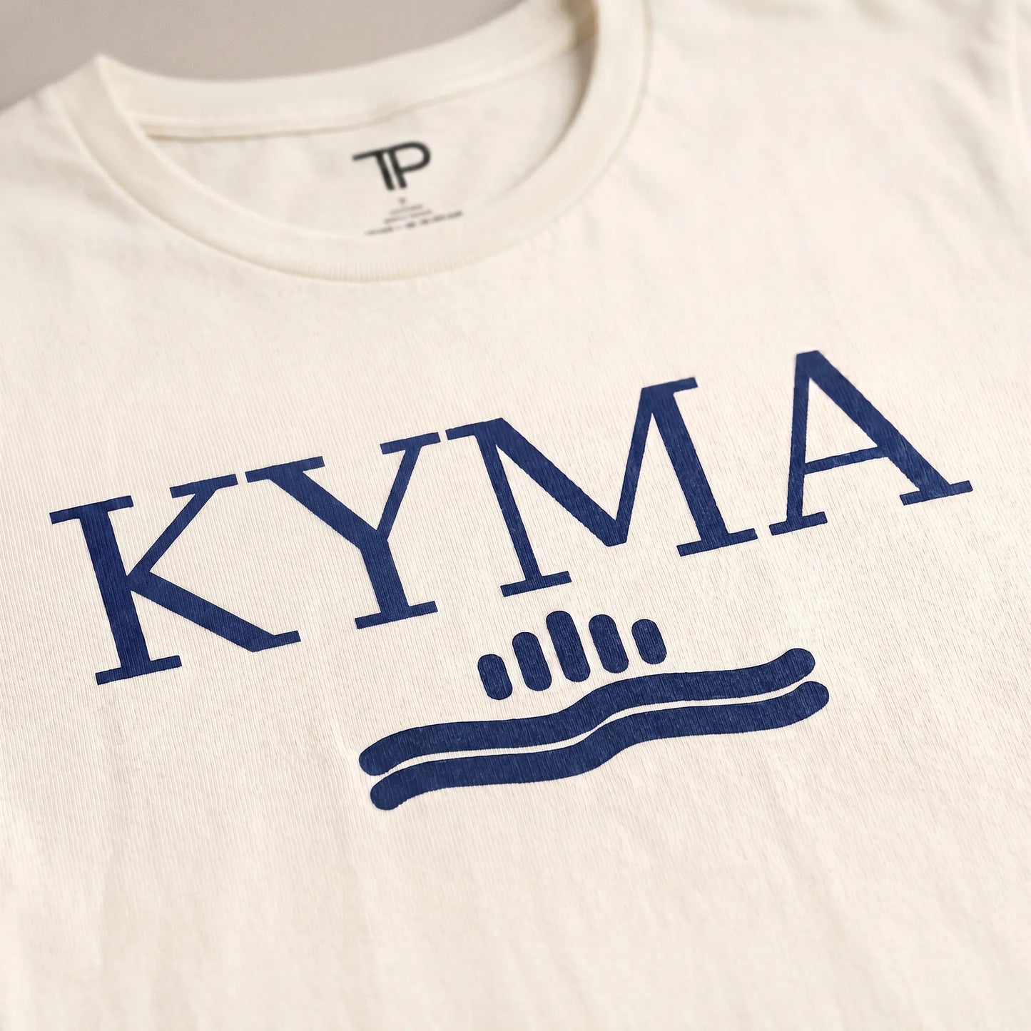 White t-shirt with blue 'KYMA' logo on a white background