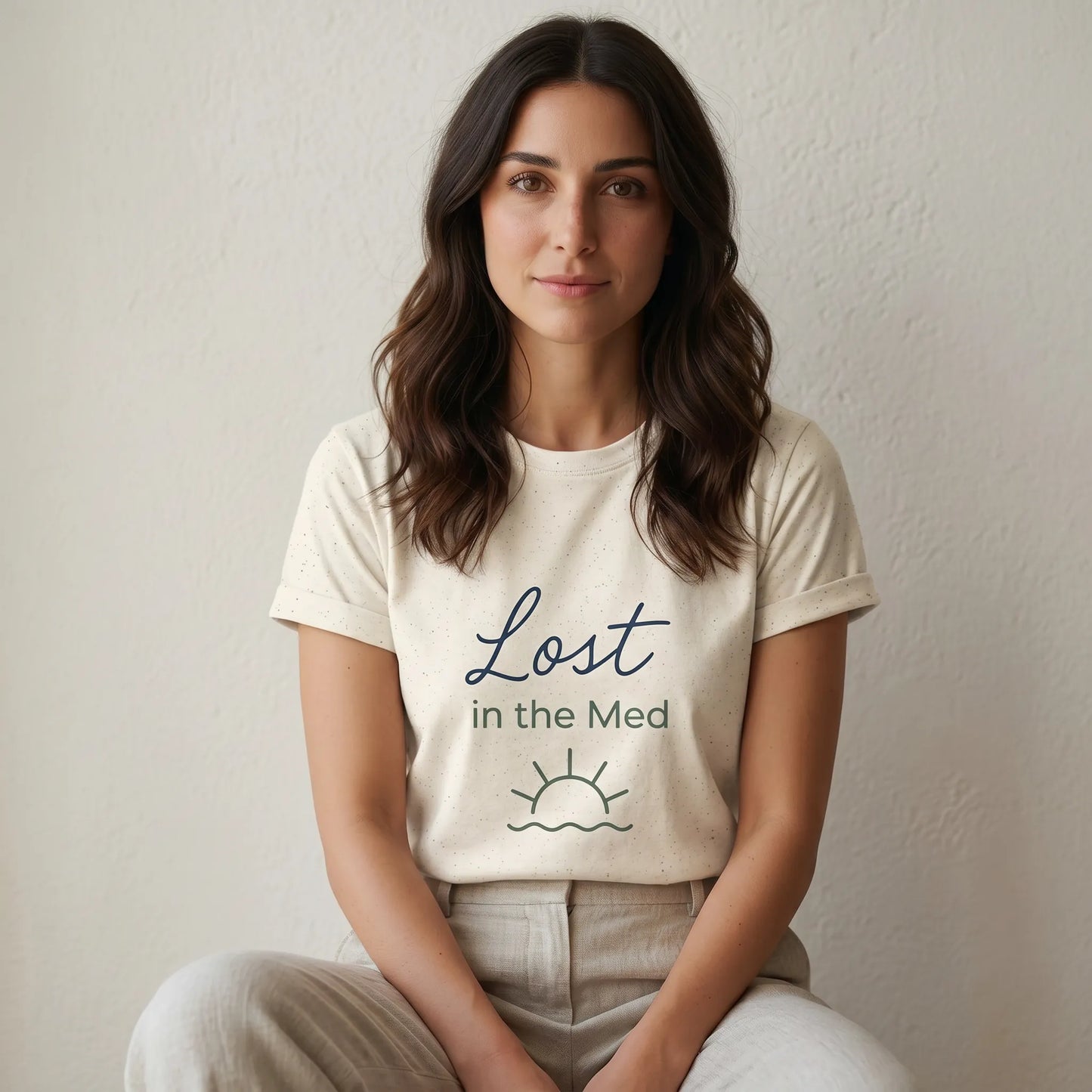 Woman wearing a white t-shirt with 'Lost in the Med' text sitting against a plain background
