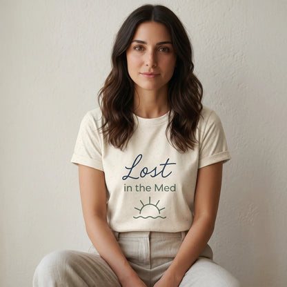 Woman wearing a white t-shirt with 'Lost in the Med' text sitting against a plain background