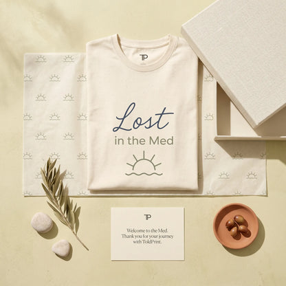 Beige t-shirt with 'Lost in the Med' design on a matching background with branded card and decorative elements.