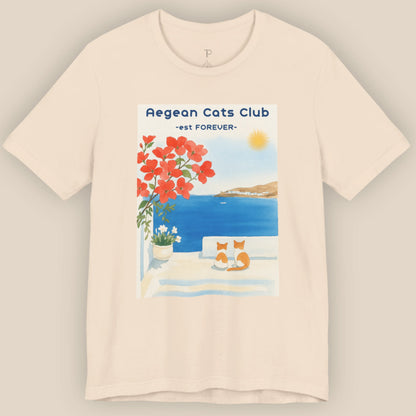 Beige t-shirt with a graphic of cats by a pool and flowers, labeled 'Aegean Cats Club'.