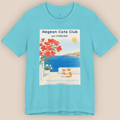 Blue t-shirt with a graphic of a cat by a beach and 'Aegean Cats Club' text on a beige background