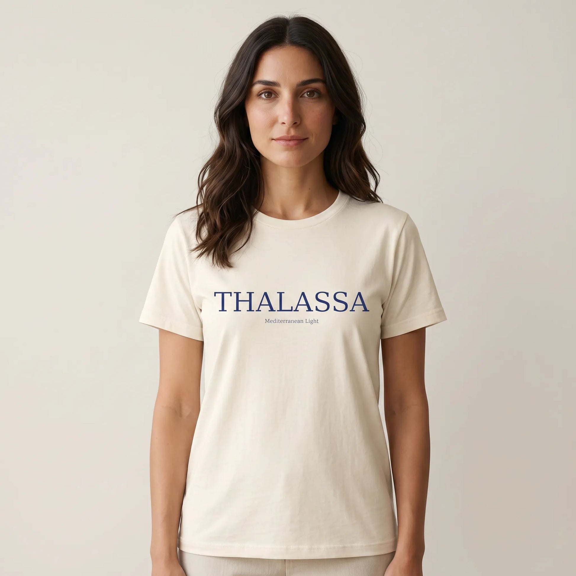Woman wearing a beige t-shirt with 'THALASSA' printed on it against a plain background