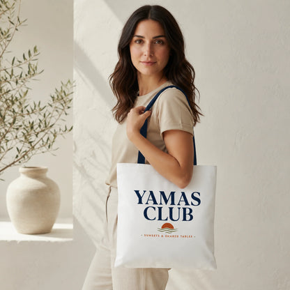 Woman holding a tote bag with 'Yamas Club' branding in a minimalistic setting.