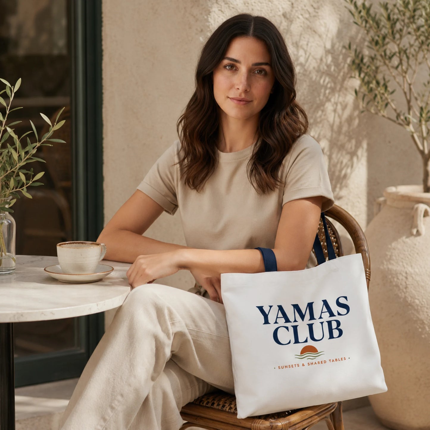 Woman sitting at a table with a cup of coffee and a 'Yamas Club' tote bag.