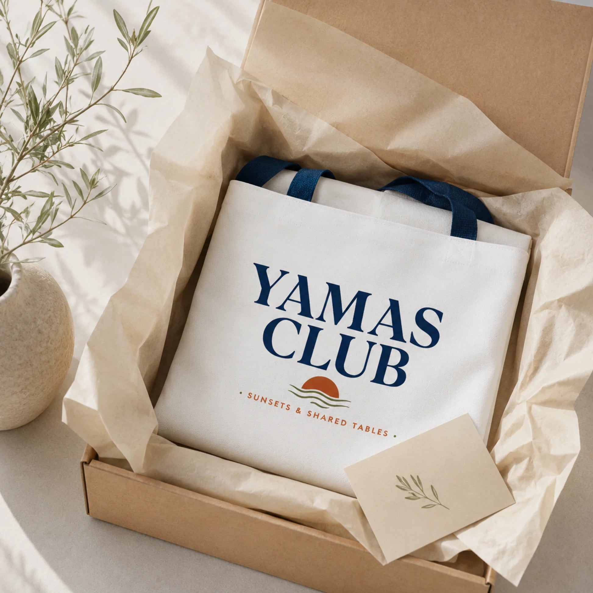 White tote bag with 'Yamas Club' text in a box with brown tissue paper.