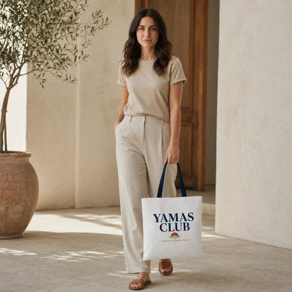 Woman holding a 'Yamas Club' tote bag in a sunlit room.