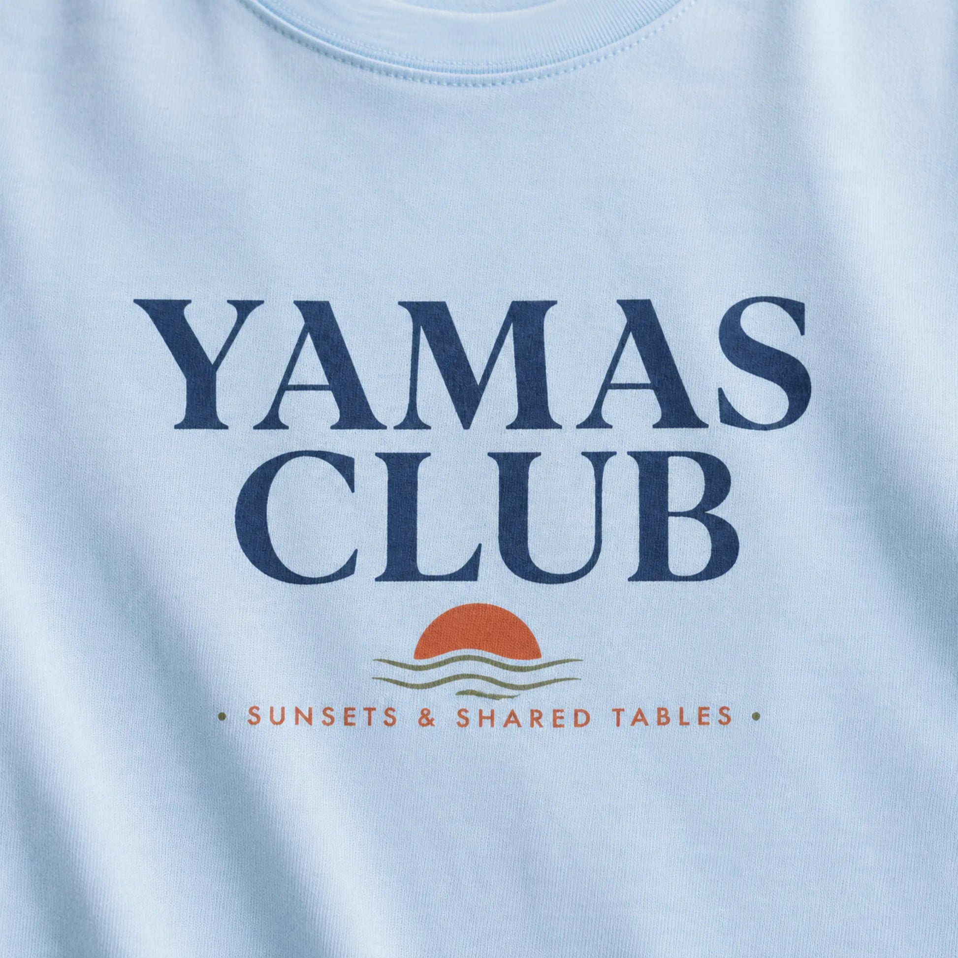 Light blue t-shirt with 'Yamas Club' text and sunset design on a white background