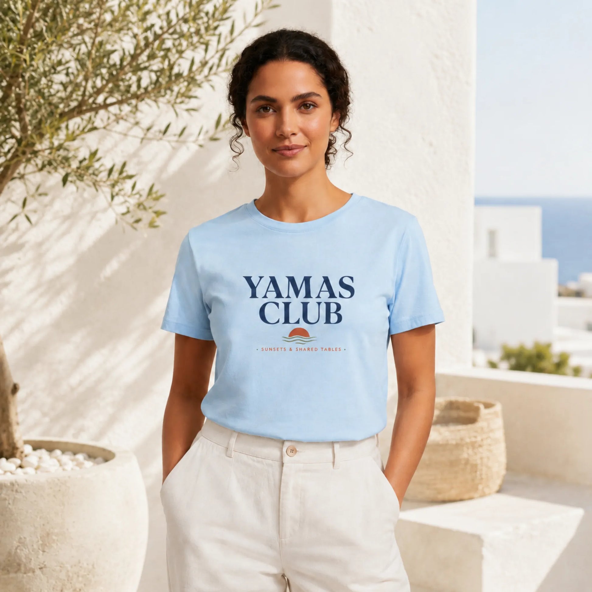 Woman wearing a light blue 'Yamas Club' t-shirt in a bright outdoor setting.