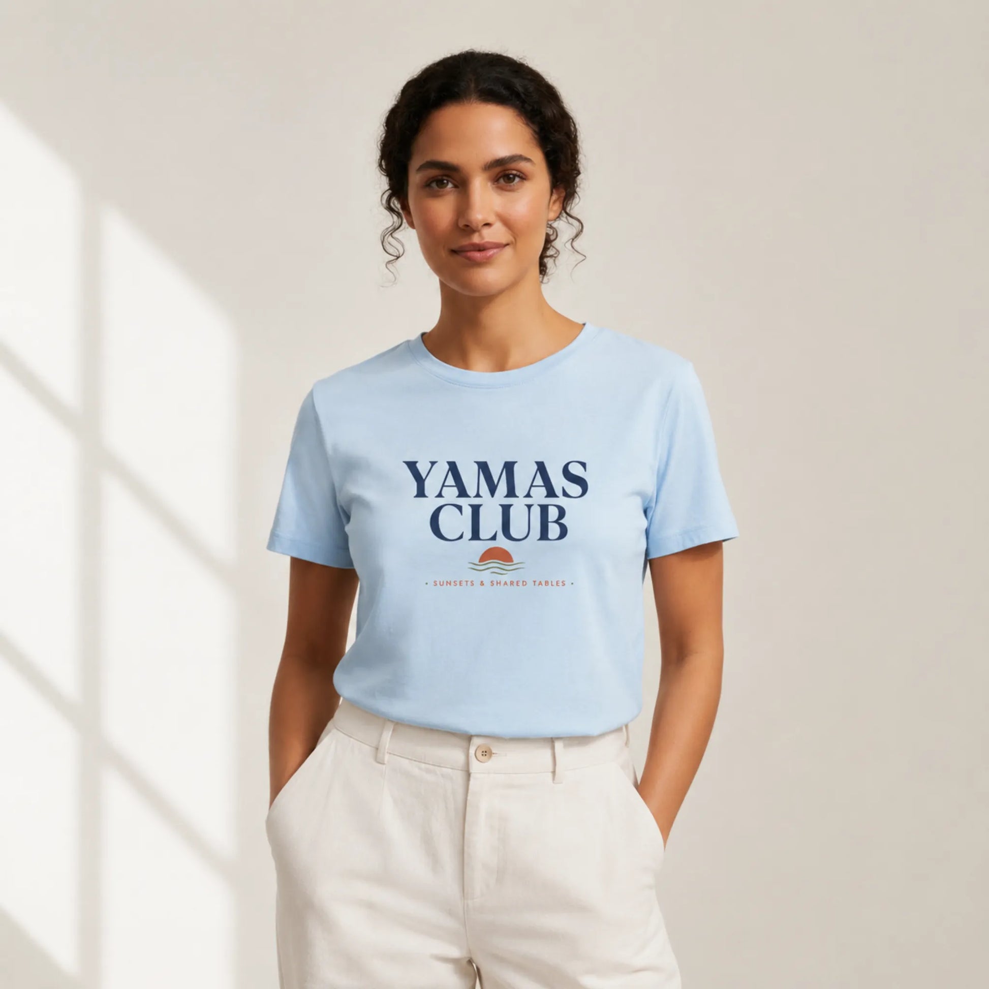 Woman wearing a light blue t-shirt with 'Yamas Club' text, standing against a neutral background